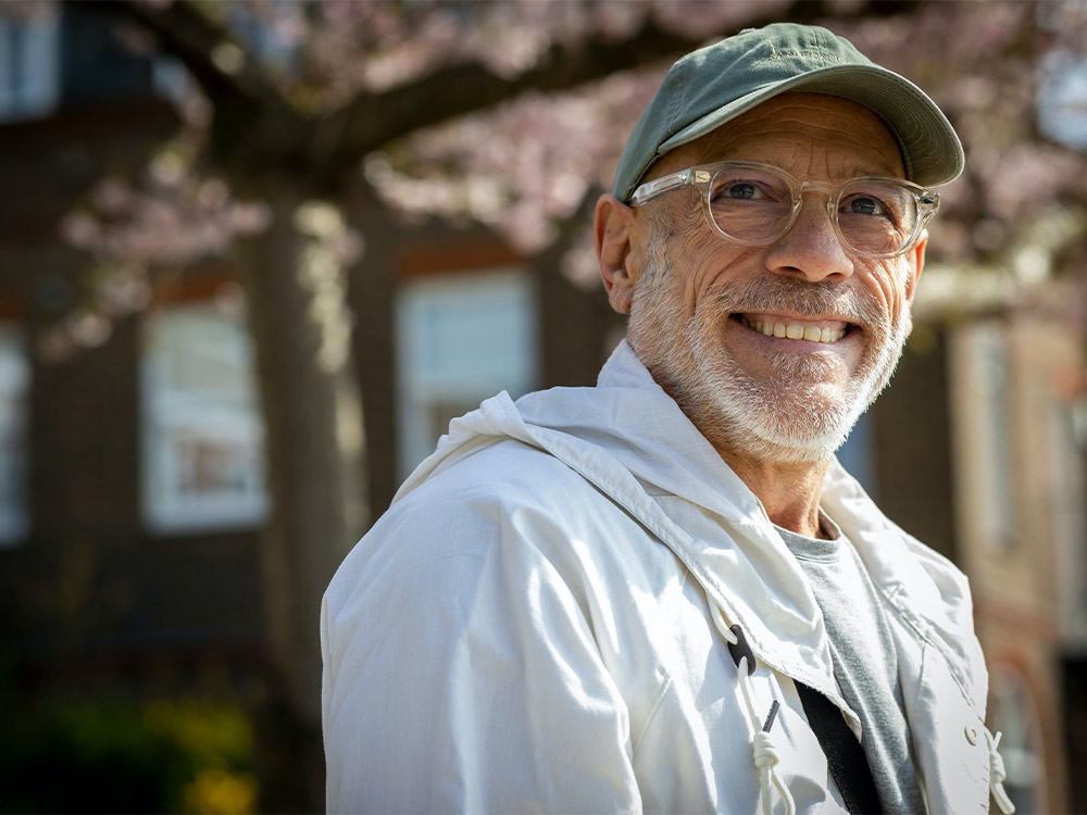 Older man smiling outside under a cherry blossom tree