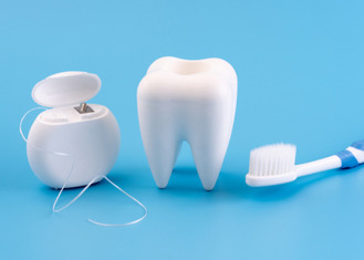 Three objects related to dental hygiene: a container of dental floss, a large model of a tooth, and a toothbrush, placed on a blue background.