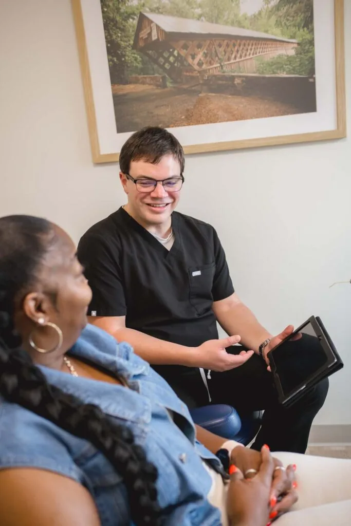 The image shows a doctor showing the patient dental procedures with the tablet his holding in a dental clinic.