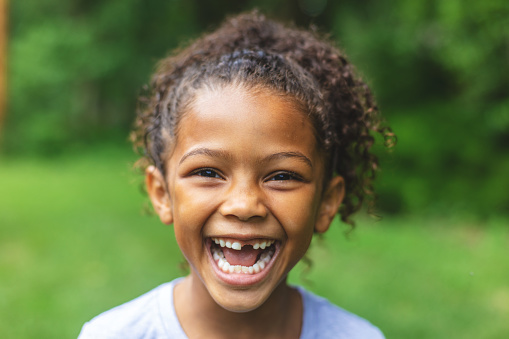 miling child outdoors showing missing front teeth, celebrating a joyful milestone in early dental development.