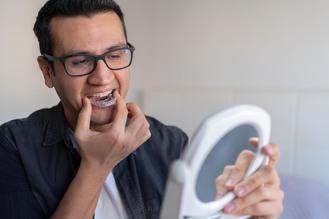 A patient uses a mirror while fitting a clear mouthguard, highlighting custom protection and comfort at Deerfoot Dental.